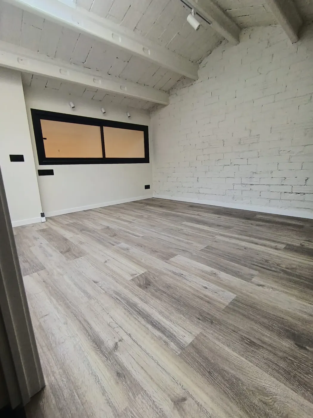 Habitación con viga vista y pared de ladrillo pintado, limpia tras el fin de obra