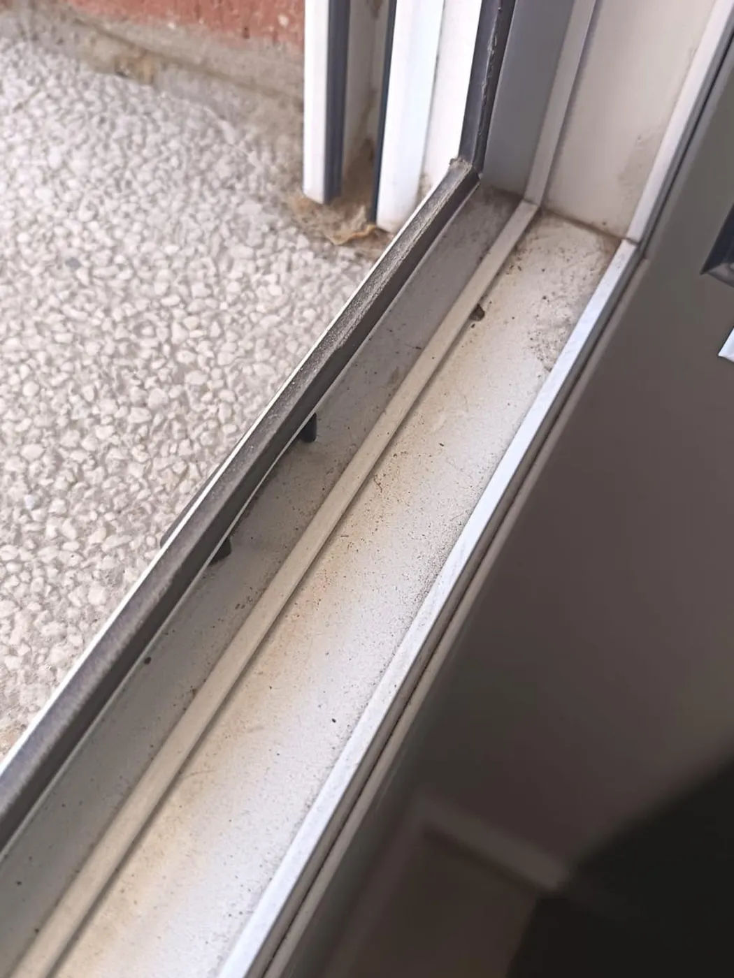 Guía de ventana corredera llena de polvo de obra y arenilla antes de la limpieza